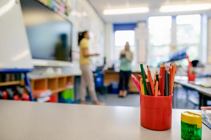 A pencil organizer is standing on a desk in a classroom.